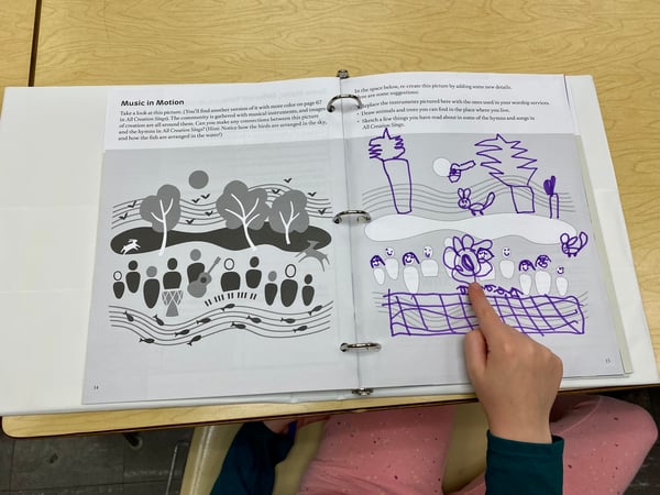 A child points to an illustration they made in their Kids Celebrate booklet